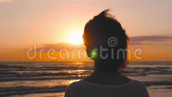 日落时站在海边望着地平线的女孩的头和肩膀的剪影视频的预览图