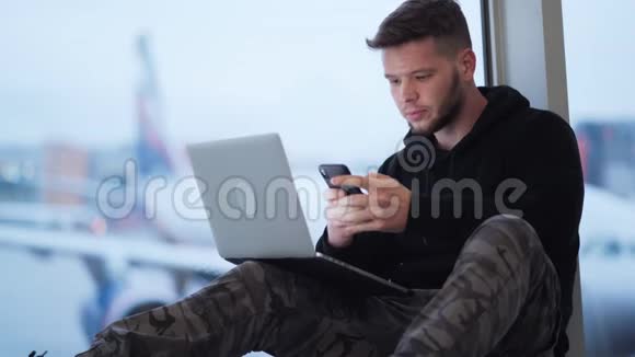 男子坐在机场使用智能手机和笔记本电脑飞机背景视频的预览图