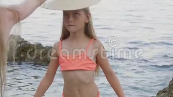 年轻的女孩穿着泳衣戴着草帽在石海海滩度假戴着帽子的微笑少女视频的预览图