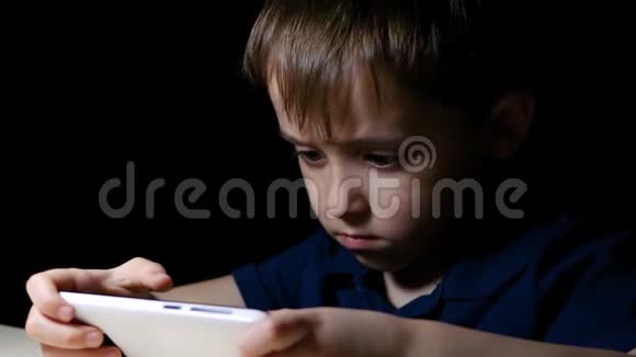 一个小男孩晚上坐在黑暗房间的桌子旁的肖像他的脸被桌灯照亮了快乐视频的预览图