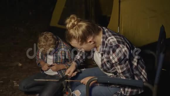 晚上游客男孩和女孩在露营地用刀子削木棍烧烤女孩和男孩青少年使用视频的预览图