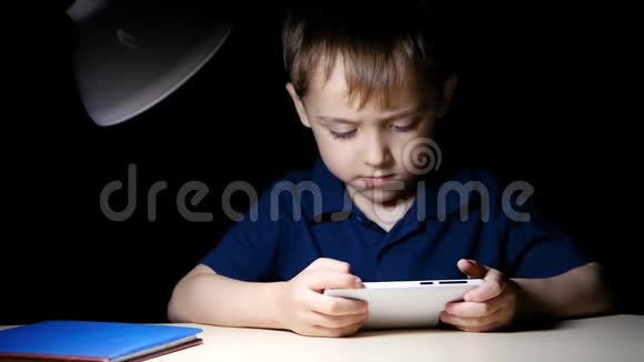 一个快乐的小男孩坐在桌子旁热情地看着他智能手机的屏幕孩子是视频的预览图