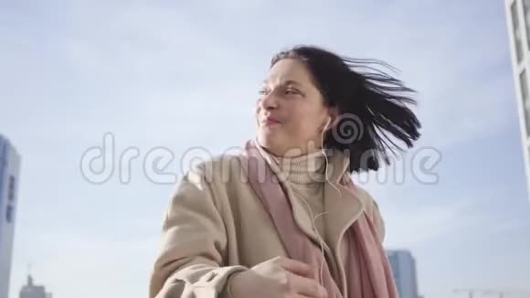 一位戴着耳机的年轻白种人女士站在城市街道上微笑着笑容满面的商务小姐视频的预览图