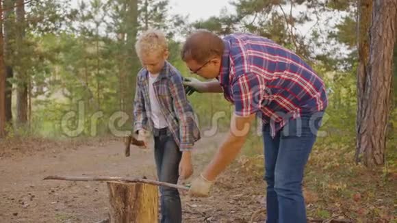 父亲教儿子在夏天的森林里用斧头砍木头爸爸和儿子十几岁的孩子在视频的预览图