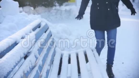 快乐有趣的年轻女人在冬天公园的长凳上擦雪慢动作视频的预览图