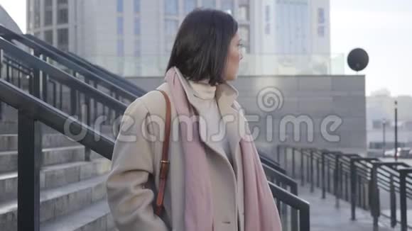 年轻白种人妇女站在楼梯上等待的肖像布吕内特商务小姐穿着优雅的米色外套视频的预览图