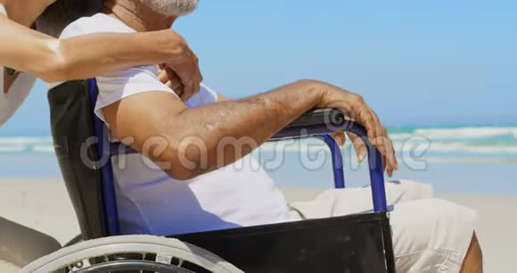 海滩上活跃的非洲裔美国老年妇女拥抱残疾老人的侧视图4k视频的预览图