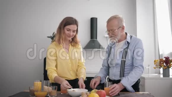 家庭关系微笑的成年女孩帮助她的老祖父从健康产品中准备维生素沙拉同时视频的预览图