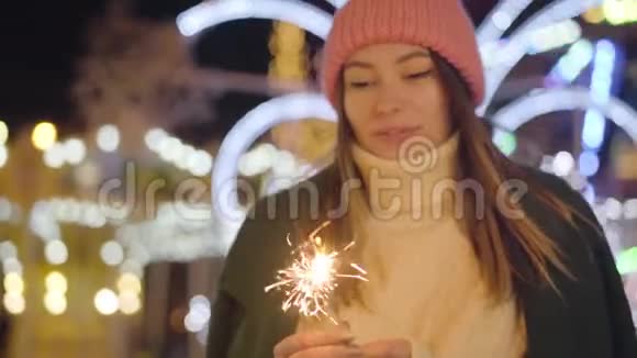 年轻微笑的白种人女人戴着粉红色帽子拿着火花的肖像快乐快乐的女孩享受城市的周末视频的预览图