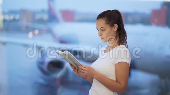 年轻女子在机场的窗户附近看书背景模糊的飞机视频的预览图