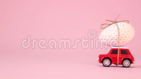 小红色玩具车引擎盖上一个金色的鸡蛋在粉红色的背景送礼物快乐复活节概念视频的预览图