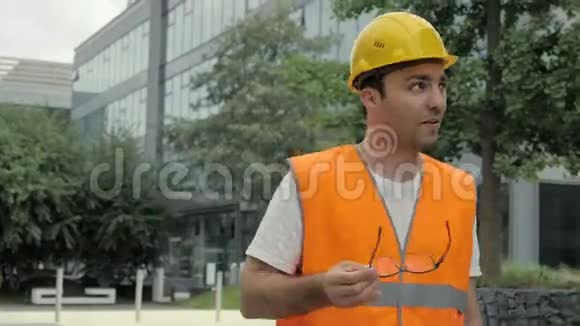 男工业工程师戴着安全帽和安全夹克沿着现代建筑走着和镜头交谈视频的预览图