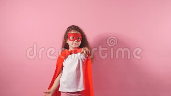 太空人的概念穿着红色斗篷戴着面具的小女孩站在粉红色背景上视频的预览图