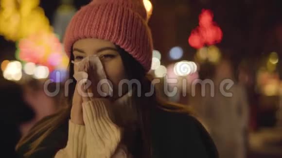 戴着粉红色帽子的病态白种人女孩在户外吹鼻子的肖像站在市集等待的年轻美女视频的预览图