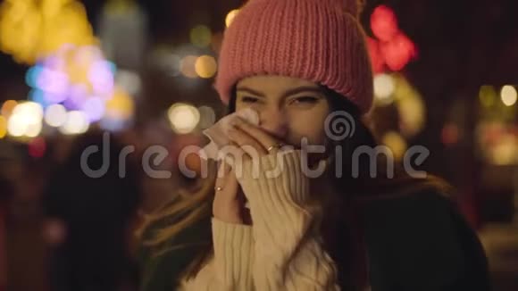 病态白种人女孩在户外摩擦鼻子和打喷嚏的肖像年轻的美女站在市集里视频的预览图