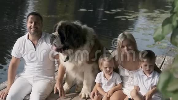 一个带着孩子和一只狗的小家庭正坐在湖边的码头上休息视频的预览图