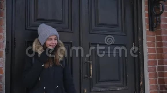 一个穿着冬装的年轻漂亮女人背景是一堵砖墙和一扇老式的门慢动作视频的预览图