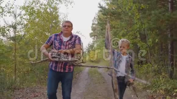 父亲和儿子在夏天的森林里露营时收集干柴友好的爸爸和儿子拿着柴火视频的预览图