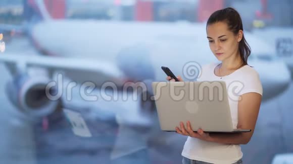 女人用手机和笔记本电脑在机场工作背景模糊的飞机视频的预览图