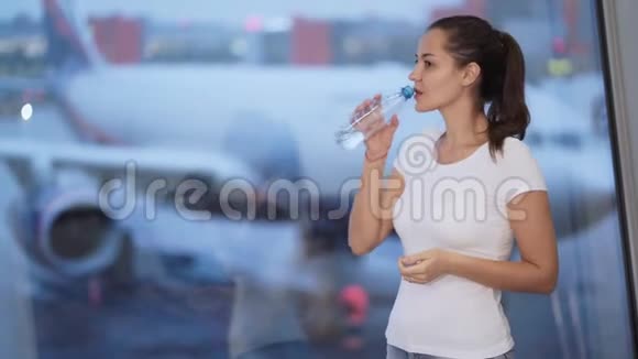 女人在机场从塑料瓶里喝水背景模糊的飞机视频的预览图