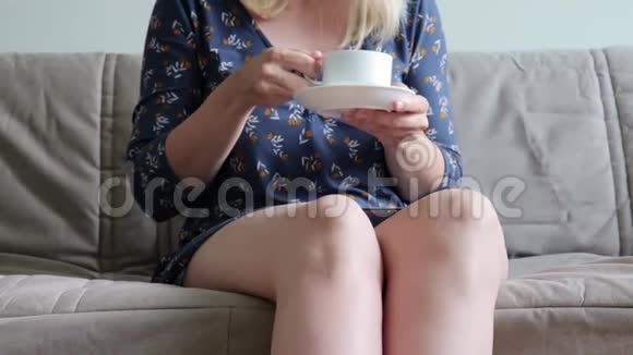 坐在沙发上坐着教练喝着热咖啡或茶穿着休闲装的女人面目全非她在做了之后很放松视频的预览图