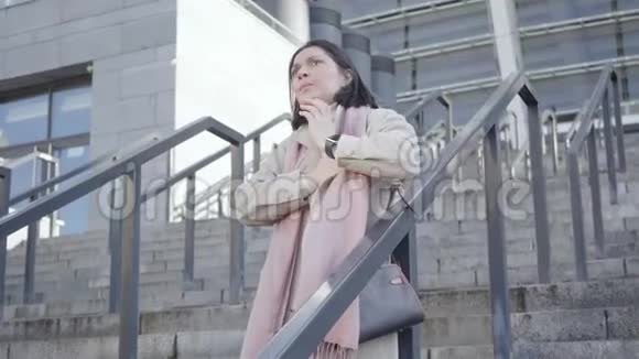 镜头接近悲伤的白种人女商人站在楼梯上双手放在胸前年轻的黑发女人视频的预览图