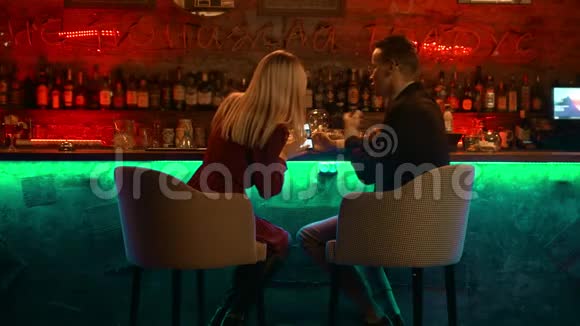 一对年轻夫妇在酒吧里约会坐在看台旁看着电话里的照片视频的预览图