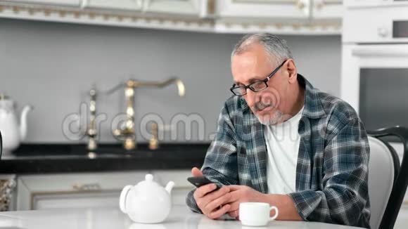 微笑着戴眼镜的成熟胡子男用智能手机聊天享受咖啡休息视频的预览图