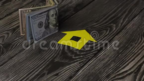在一张刷过的桌子上是美元钞票附近是一座用纸剪成的房子的轮廓一个男人把一串钥匙视频的预览图