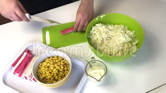 男人做沙拉切片蟹棒在切割板上容器旁边是碎北京白菜玉米和蛋黄酱视频的预览图