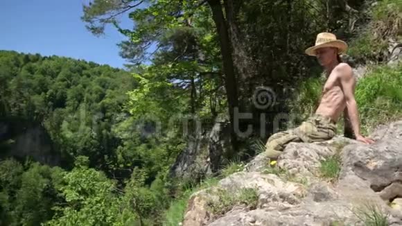 赤裸躯干的人坐在悬崖上向下看夏天晴天全景视频的预览图