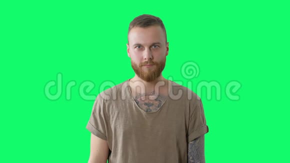 严肃的帅哥在铬钥匙上自信而惊讶的留着胡须的纹身嬉皮士正在看绿色的相机视频的预览图
