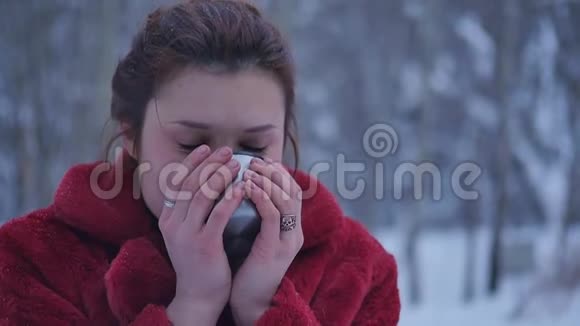 一个女人正在雪地森林里喝热茶或咖啡一个漂亮的女孩想在冬天取暖视频的预览图