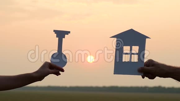 日落时纸屋模型的剪影一个男人和一个女人拿着纸房子和钥匙背景是视频的预览图