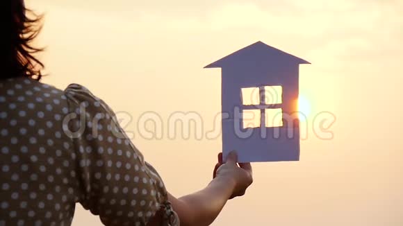 女孩手里拿着纸房子的模型日落时太阳的光芒穿过太阳的窗户视频的预览图