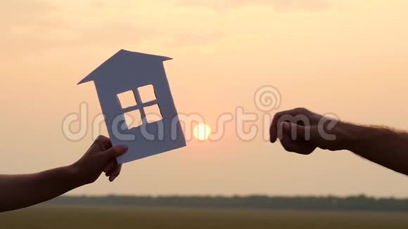 一男一女在夕阳的背景下互相传递一个纸房子的模型房地产概念视频的预览图