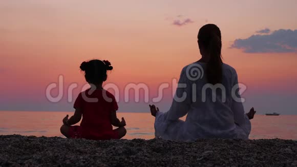母亲和她的小女儿一边欣赏日落一边在海边或海边沉思视频的预览图