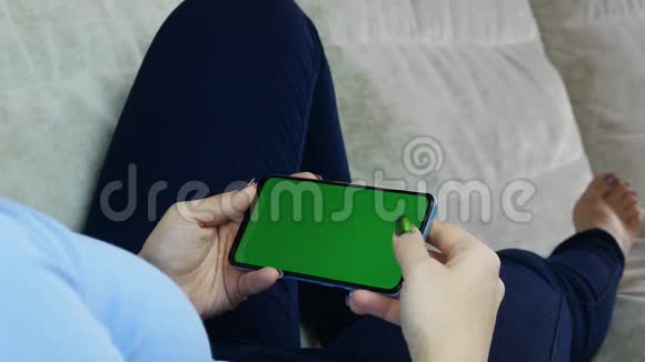 在家的女人用预先键好的绿色屏幕轻松阅读智能手机视频的预览图