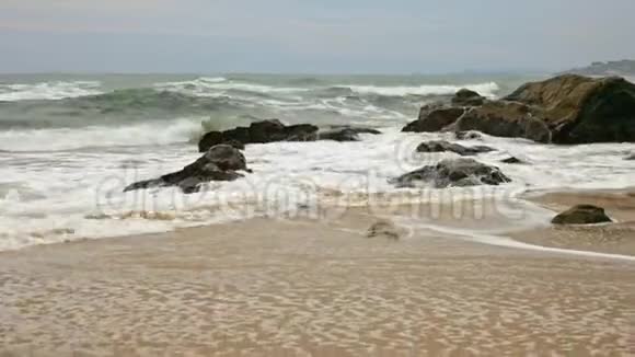 海浪在沙质海岸的岩石上破碎视频的预览图