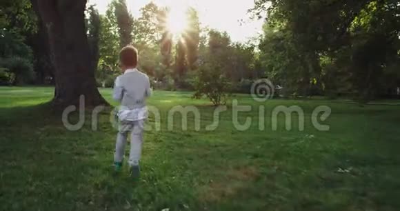 5岁的男孩在公园中央跑着带着一个球穿过绿草享受着童年视频的预览图