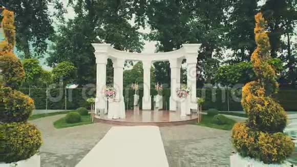 向后鸟瞰美丽的婚礼白色拱门和美丽的绿色公园区地毯视频的预览图