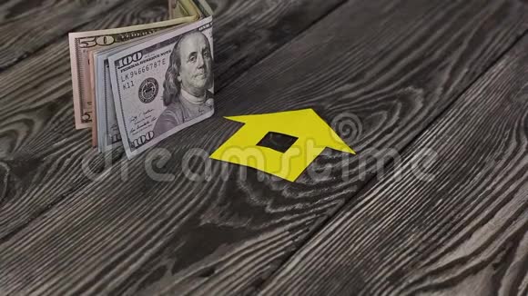 在一张刷过的桌子上是美元钞票附近是一座用纸剪成的房子的剪影一个男人放了一个钱包和一个视频的预览图