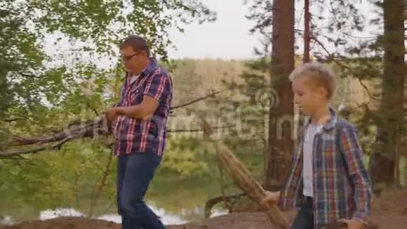 父亲一起儿子少年背着干柴在夏天的森林里生火爸爸和儿子准备木柴和视频的预览图