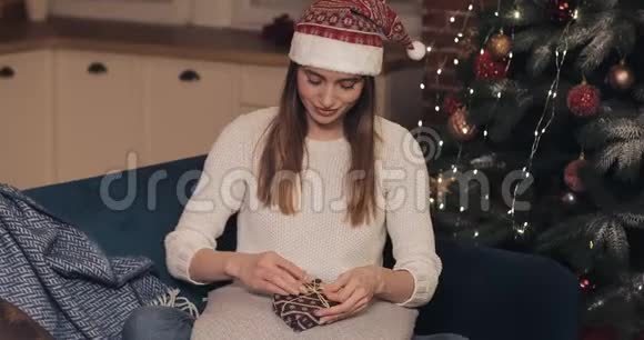 一位穿着毛衣戴着圣诞帽坐在沙发上靠近圣诞树的漂亮女孩最后敲定了一个小小的视频的预览图