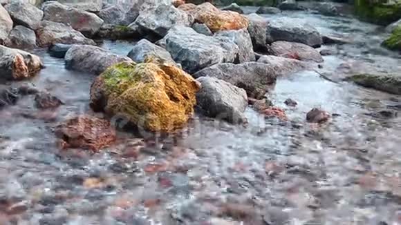 在阳光明媚的日子里快速的水以不同大小的石头流动视频的预览图