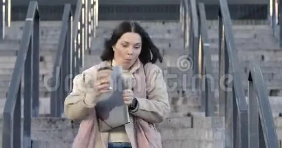 一位深黑肤色的白种人妇女带着咖啡杯和文件夹从楼梯上跑下来看着文件视频的预览图
