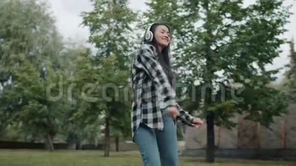 夏天在公园跳舞的快乐亚洲女人戴着耳机玩得开心视频的预览图