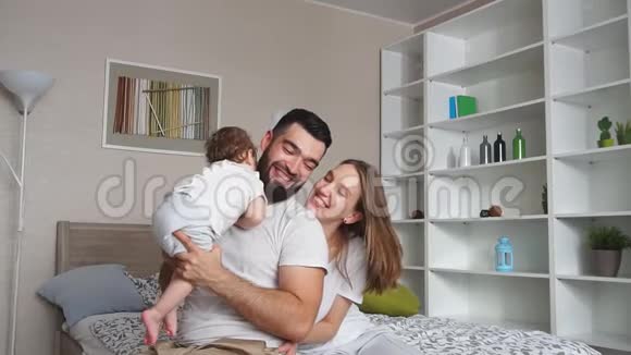 年轻的大胡子父亲把女儿举在头上母亲坐在床上看着家人视频的预览图