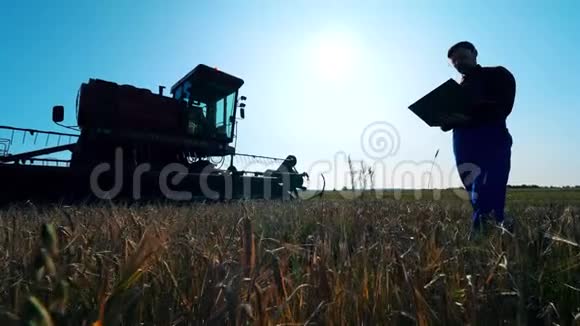 农场工人站在田里的拖拉机旁用手提电脑打字视频的预览图