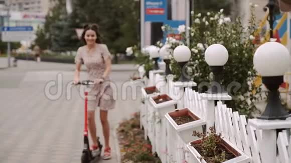 美丽的女孩骑着电动滑板车在街道人行道上视频的预览图